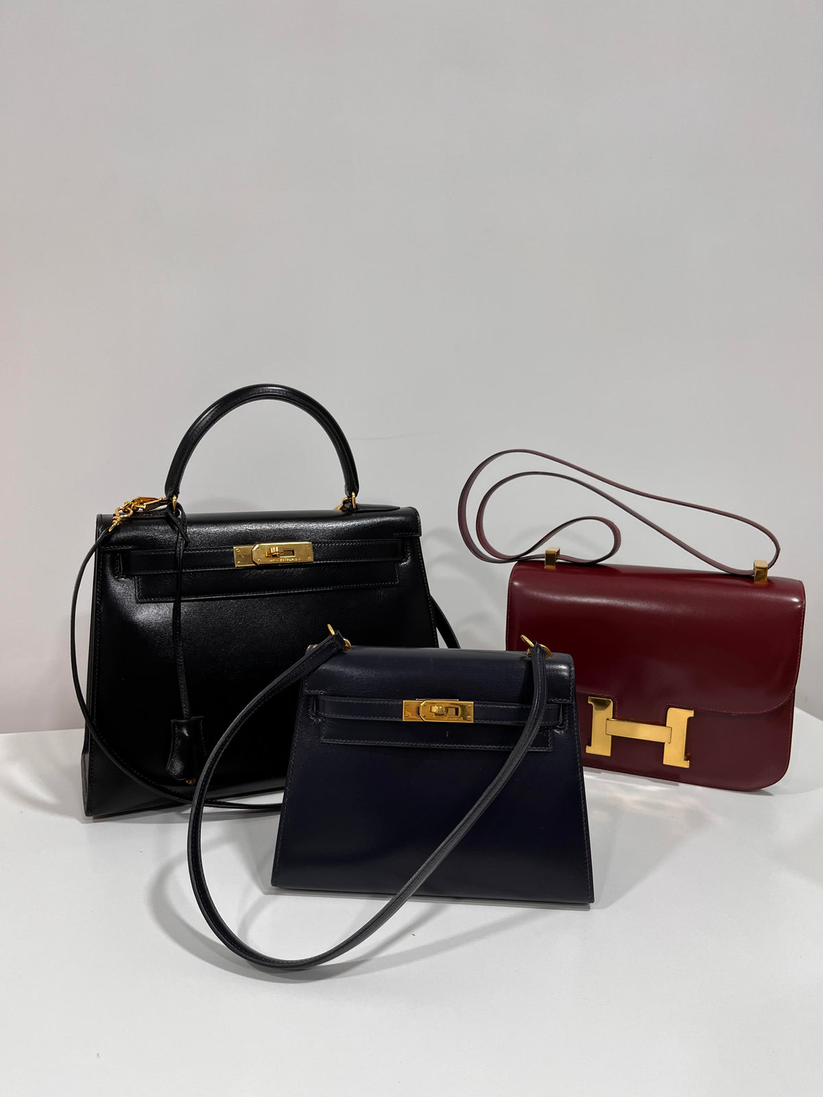 Featuring vintage Hermès Kelly bags in black and navy box calf, with a Rouge H burgundy Constance 23